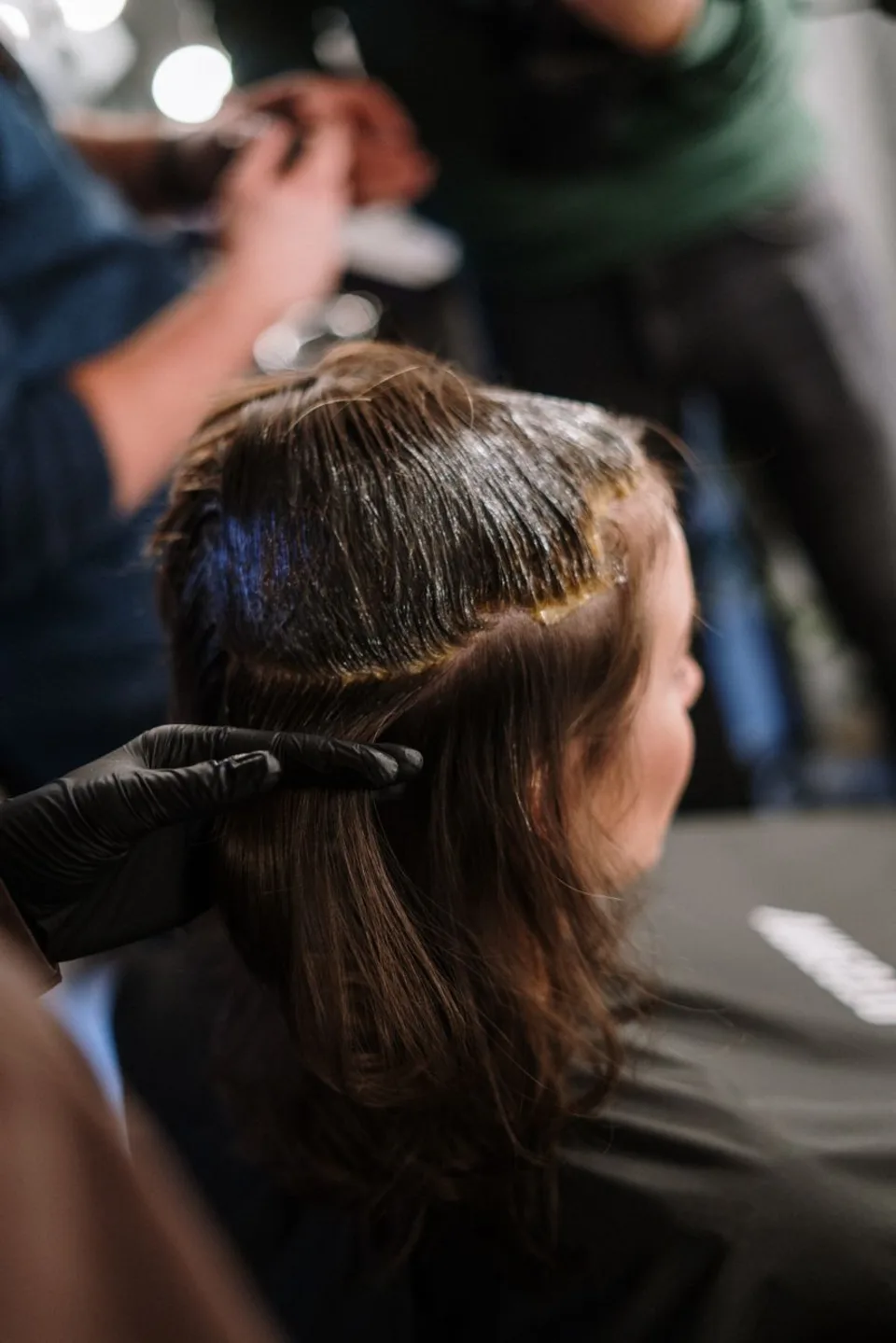 Mano con guante separando una sección de cabello castaño largo, vista desde atrás